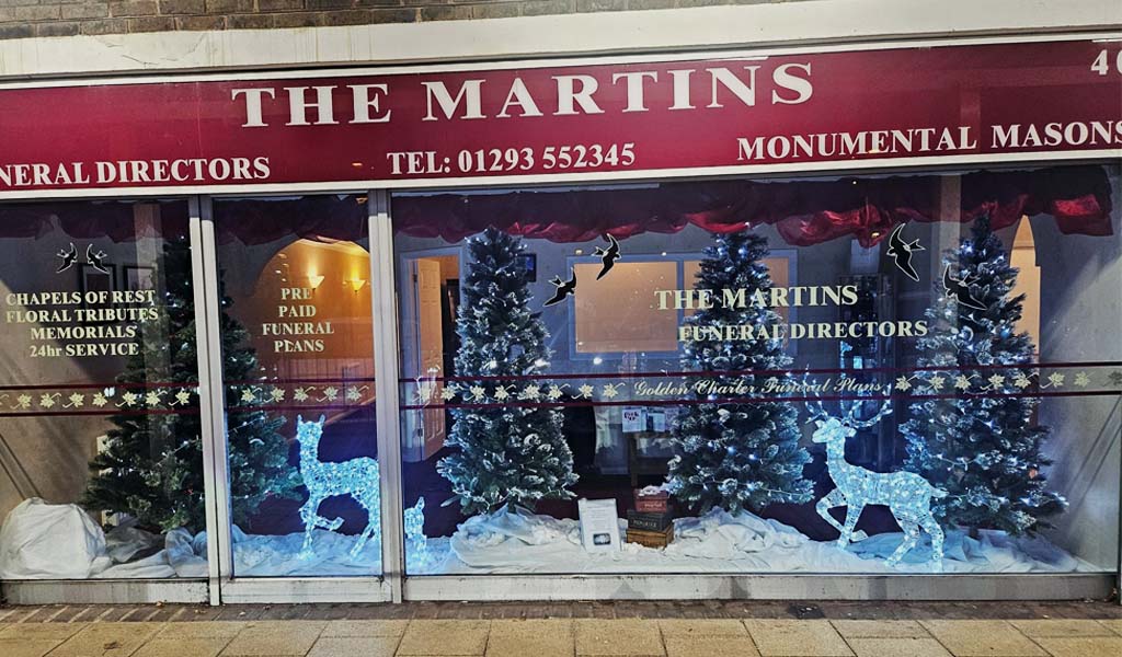 The Christmas window display of The Martins. There are four Christmas trees and light up blue deer with snow on the ground in the window.